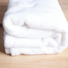 White flannel throw blanket with a fluffy texture folded on a wooden surface.