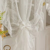 White sheer curtain with ruffled lace trim tied in a bow, hanging on a white wooden door.