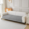 A white sofa covered with a gray quilted anti-slip fabric, set in a bright room.