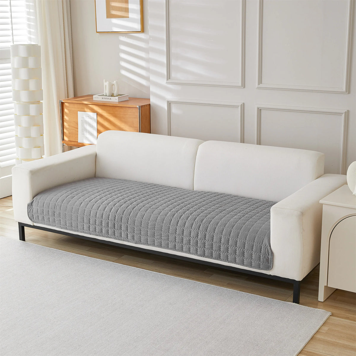 A white sofa covered with a gray quilted anti-slip fabric, set in a bright room.