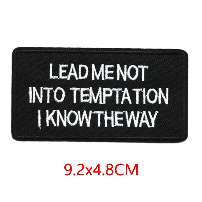 Black iron-on embroidered letter patch with white text that reads Lead me not into temptation I know the way