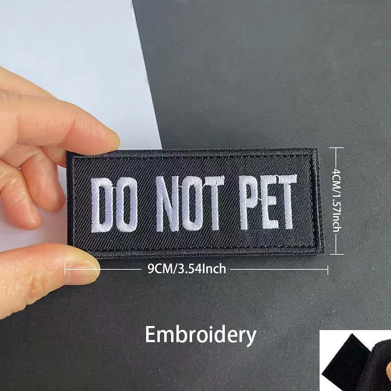 A black embroidered patch with white text DO NOT PET is held by a hand against a dark background.