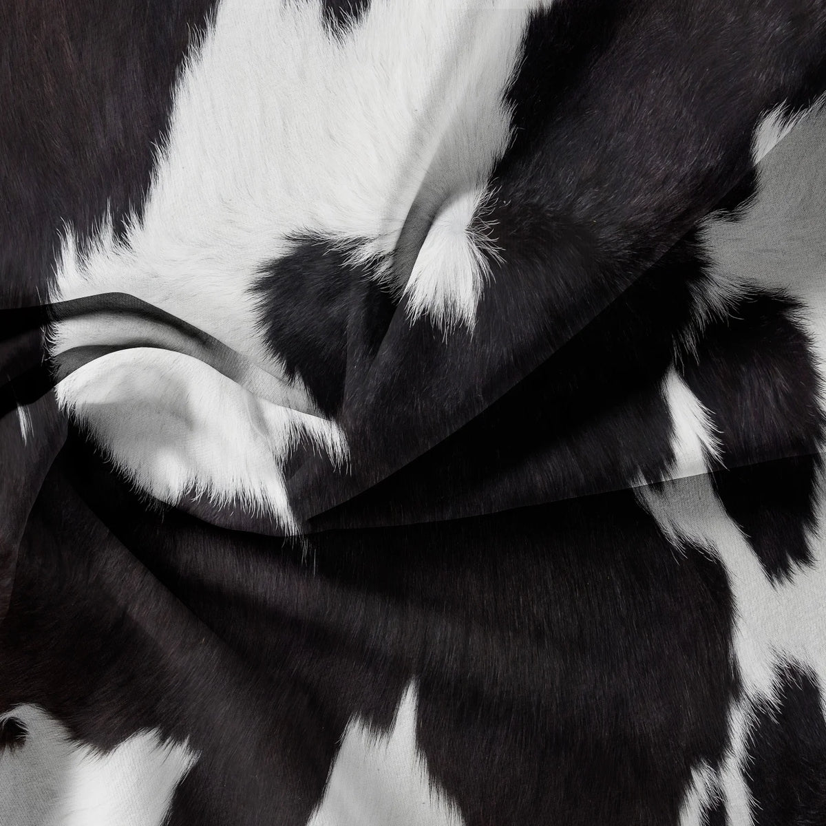 A close-up of a black and white cow print yak leather duvet cover fabric draped in soft folds.