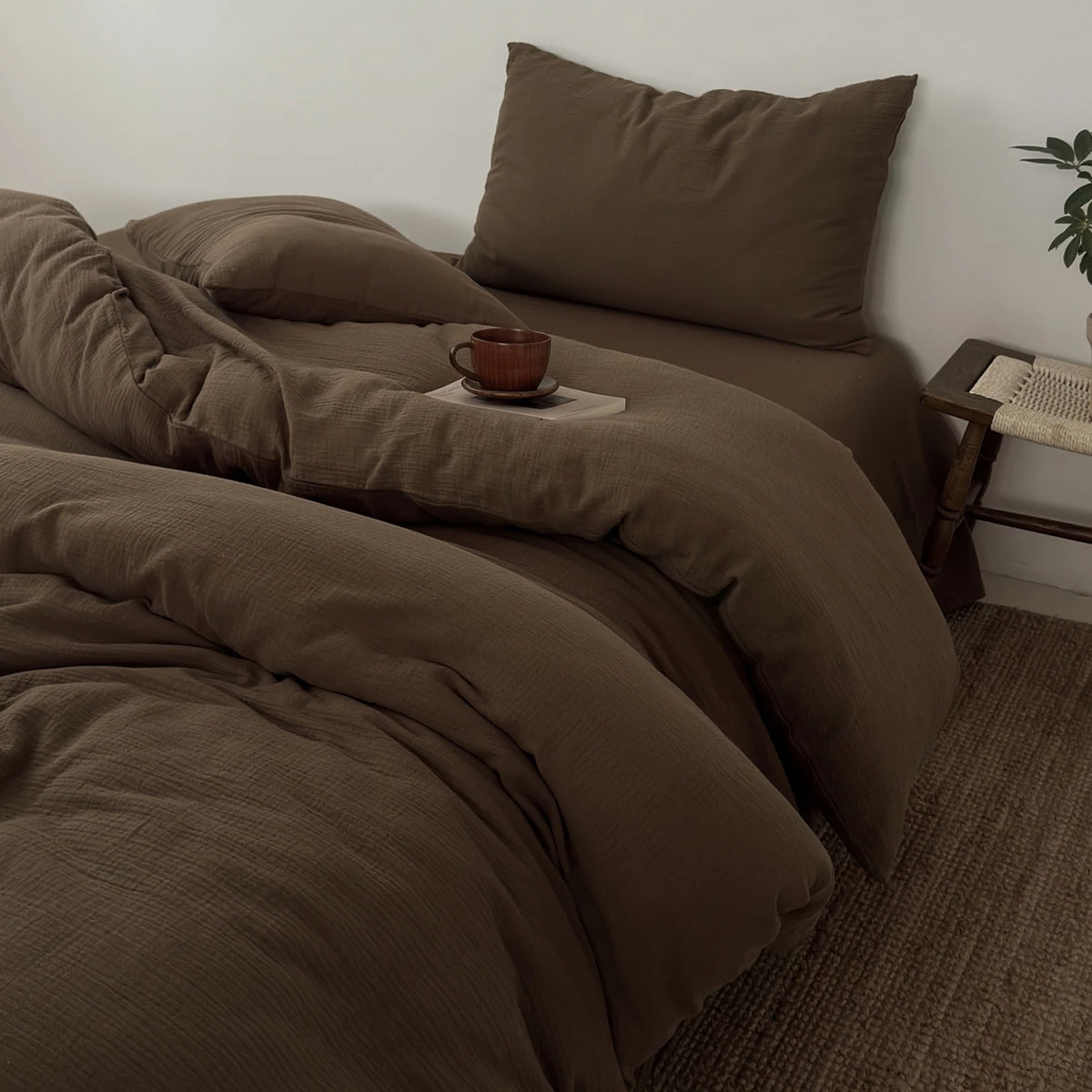 A dark brown duvet cover set with matching pillows and a small cup on a bed.