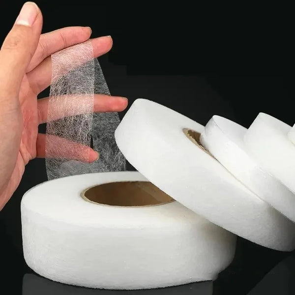 A hand holds a roll of double-sided iron-on adhesive tape for garment repair, showing the clear tape and the white roll.