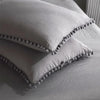 A white duvet cover set featuring pom-pom trim on the corners, resting on a bed.