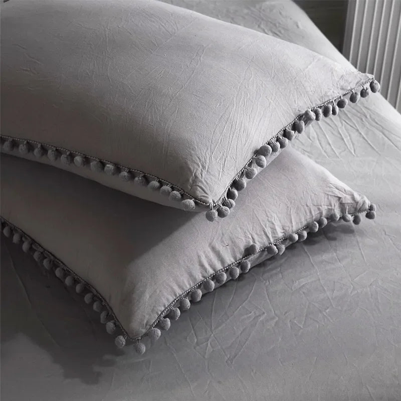 A white duvet cover set featuring pom-pom trim on the corners, resting on a bed.