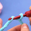 A hand is holding a red crochet hook with a light blue yarn loop against a purple background.