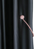 A close-up of a pink magnetic curtain tieback with a spherical top attached to a cord, against a dark gray fabric.