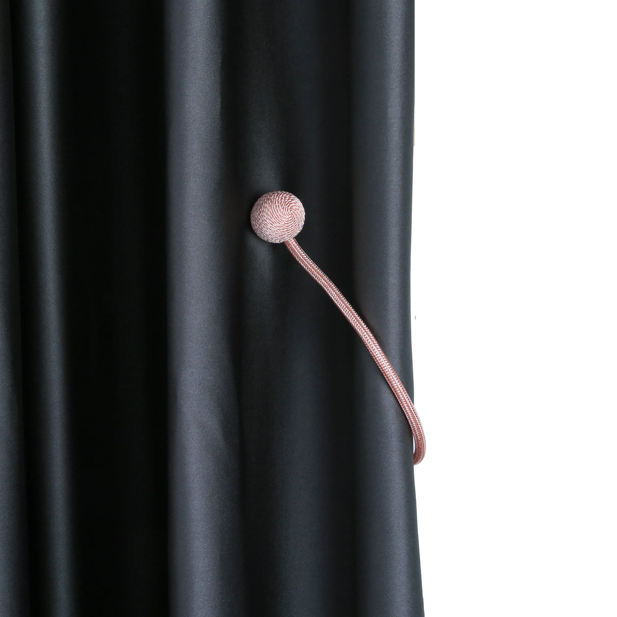 A close-up of a pink magnetic curtain tieback with a spherical top attached to a cord, against a dark gray fabric.