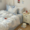 A bed with a light blue duvet cover featuring a white floral pattern, pillows, and a bedside table.