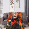An orange and black patterned throw blanket draped over a gray sofa in a brightly lit room.