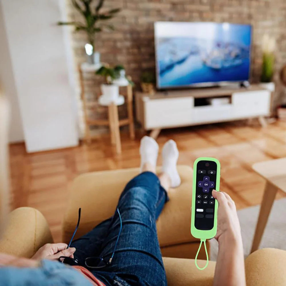 A hand holds a lime green silicone remote cover with a lanyard, resting on a couch.