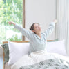 A woman is smiling while lying in a bed with white pillows and green bedding.