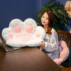A woman is sitting at a wooden desk with a white plush bear paw cushion and a laptop in front of her.