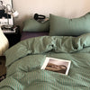 A close-up of a green and white striped duvet cover set on a bed with pillows and a lamp.