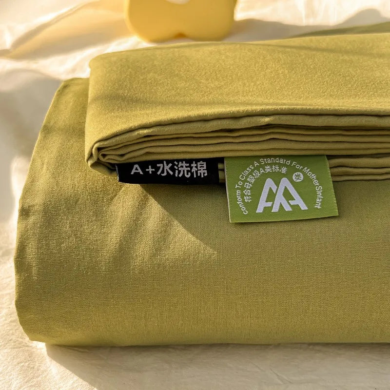 A stack of olive green organic cotton bedding, including a flat sheet and pillowcases, with a tag visible.