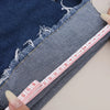 A close-up of denim fabric showing a measuring tape placed along the edge and frayed detail.