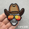 An embroidered iron-on patch featuring a skull and crossbones design on a brown cowboy hat.