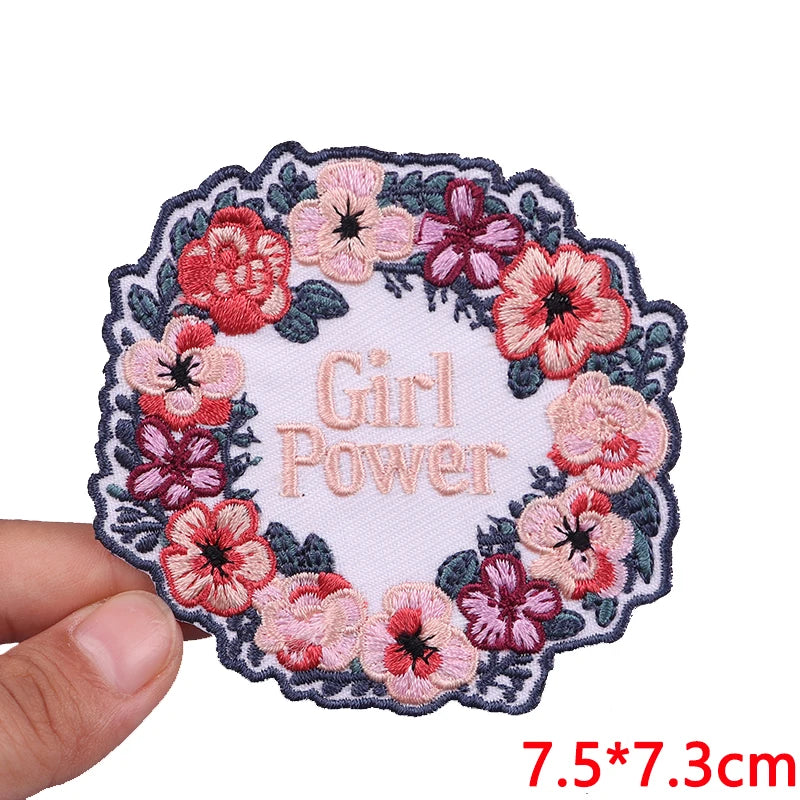 Pink and red floral embroidery patch with the text Girl Power on a white fabric background
