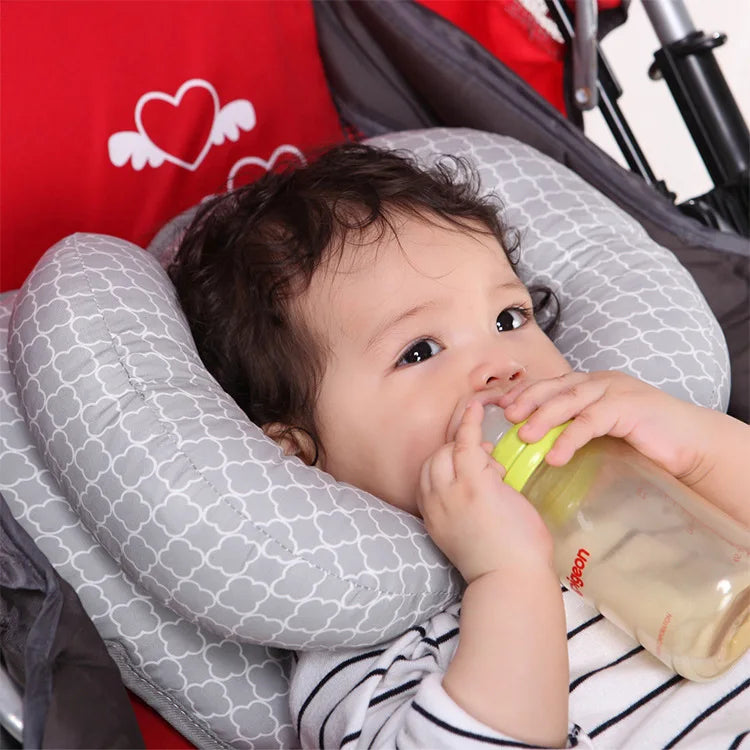 A baby is resting on a gray head and neck support pillow inside a stroller or car seat.