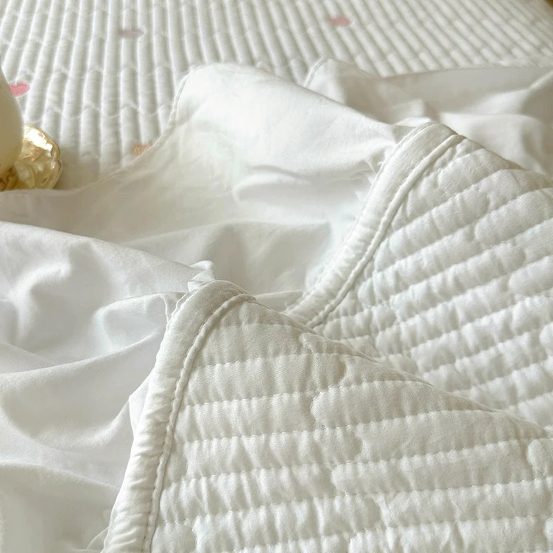 White quilted bedding set with subtle floral embroidery on a bed.