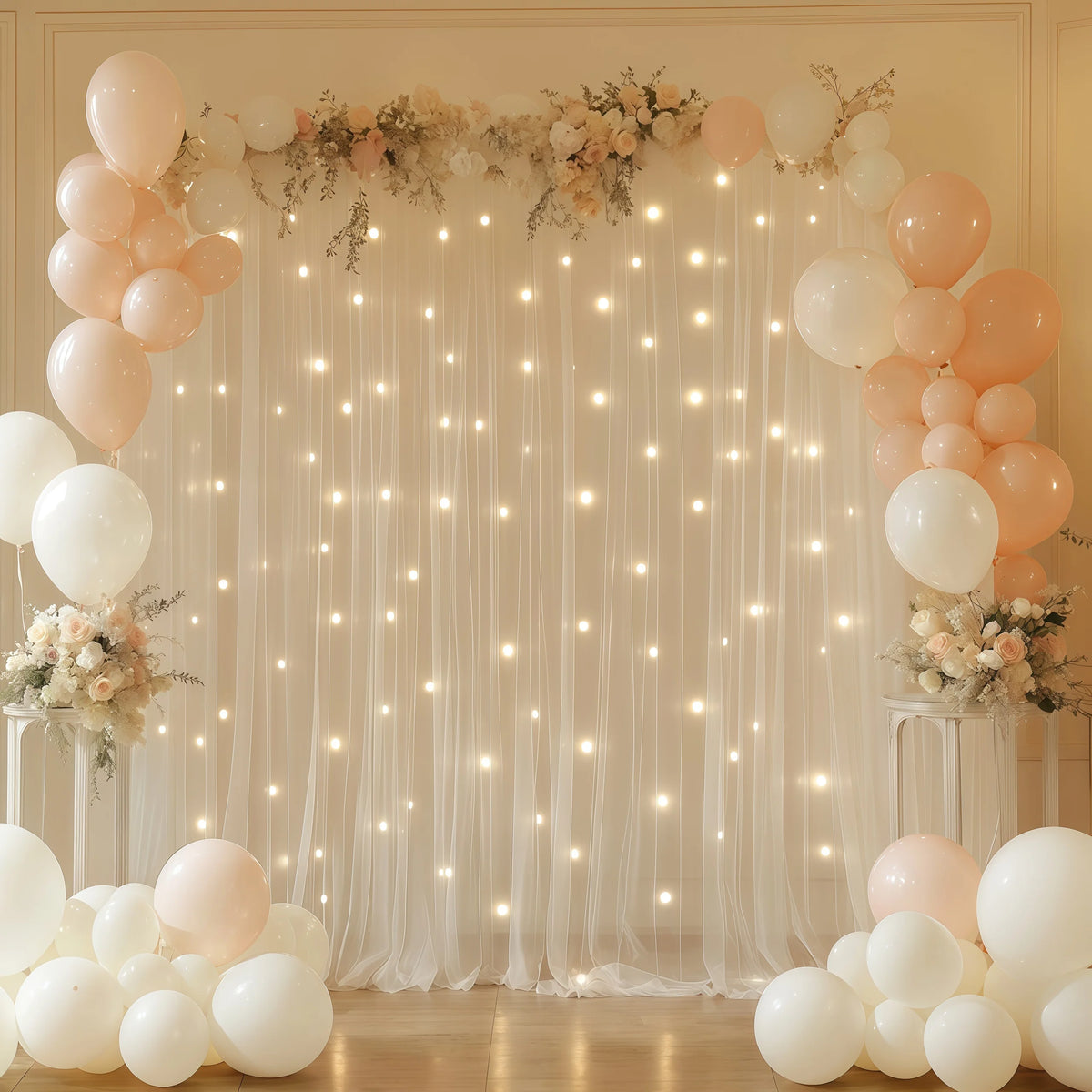 A sheer white tulle backdrop decorated with warm fairy lights and clusters of pink and white balloons for an event.