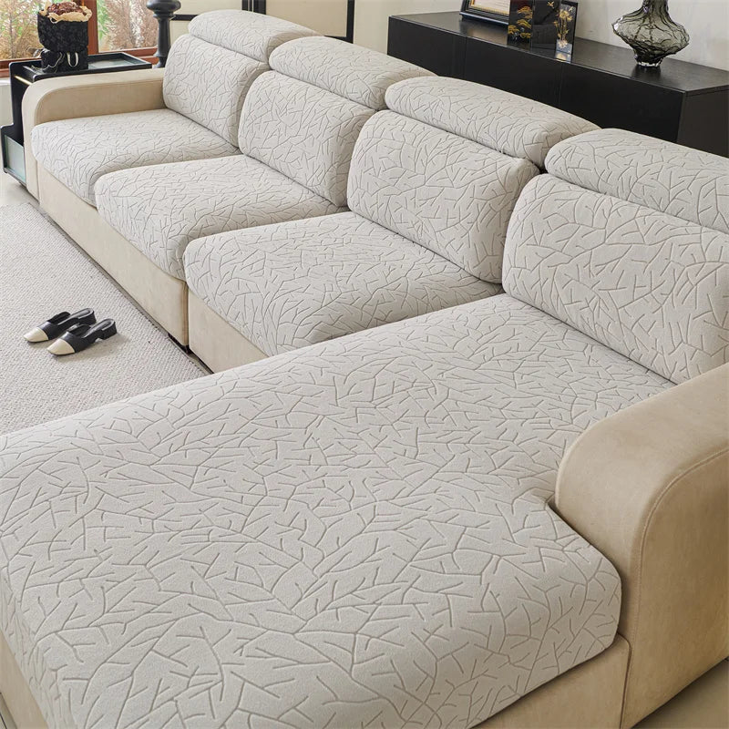 A light beige patterned jacquard sofa cover featuring a textured, branching design on a sectional sofa.
