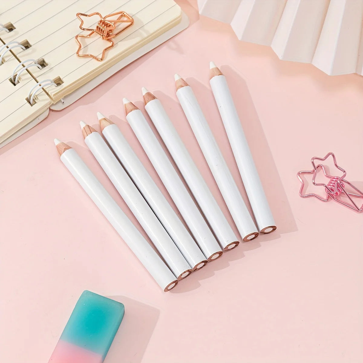A collection of white bamboo chalk pencils with pink accents are arranged on a light pink surface next to a wooden ruler and 