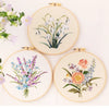 Three circular embroidery hoops displaying floral patterns on light fabric.