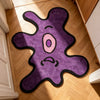 A purple and black playful one-eye monster area rug placed on a light wood floor.