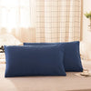 A set of two navy blue soft polyester pillow covers resting on a beige bed.
