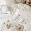 A white embroidered rose duvet cover set displayed on a bed with soft lighting and a magazine.