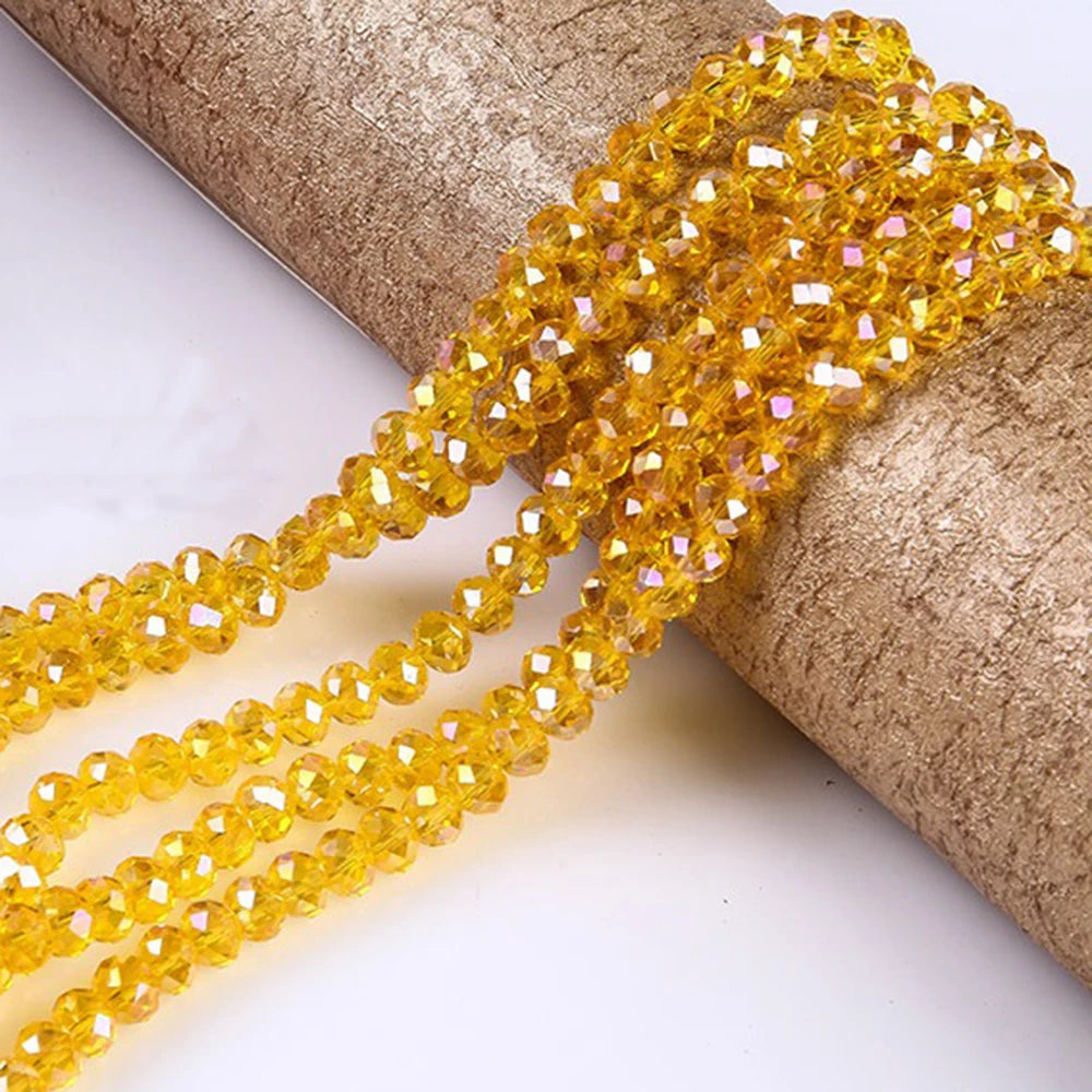 A close-up of yellow faceted rondelle glass beads strung together, resting on a cylindrical object.