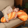 An orange French bread plush pillow resting on a beige sofa.