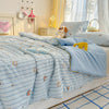 A light blue quilt with a cartoon pattern featuring small orange and yellow animals is displayed on a bed.