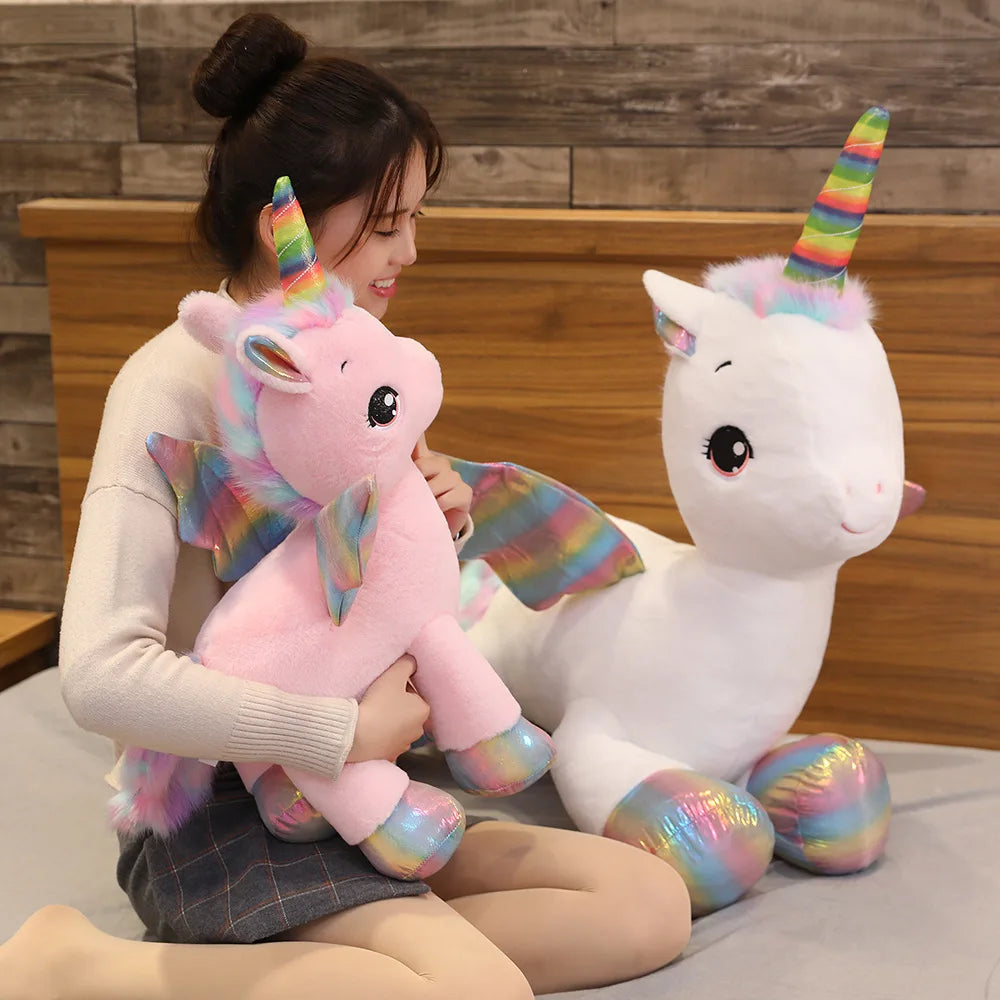 A woman is holding a pink unicorn plush toy with iridescent accents against a wooden background.