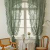 Pair of sheer sage green lace curtains framing a window with a white table and chairs.