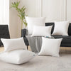 A collection of white and black square cushions displayed on a dark sofa with a striped throw blanket.