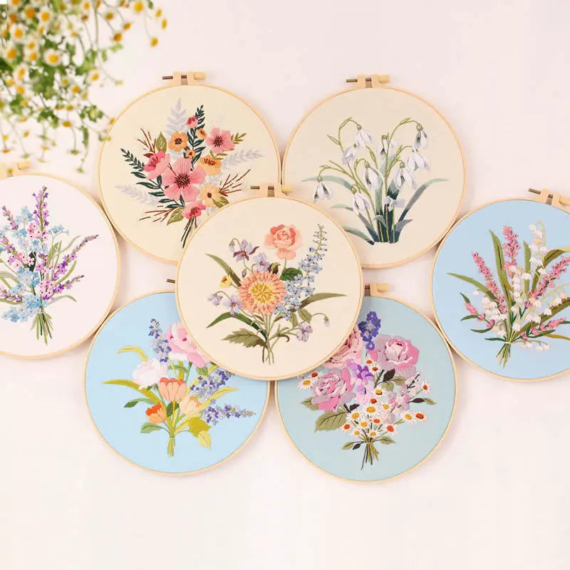 A collection of six round embroidery kits featuring various floral patterns on light wood backgrounds.