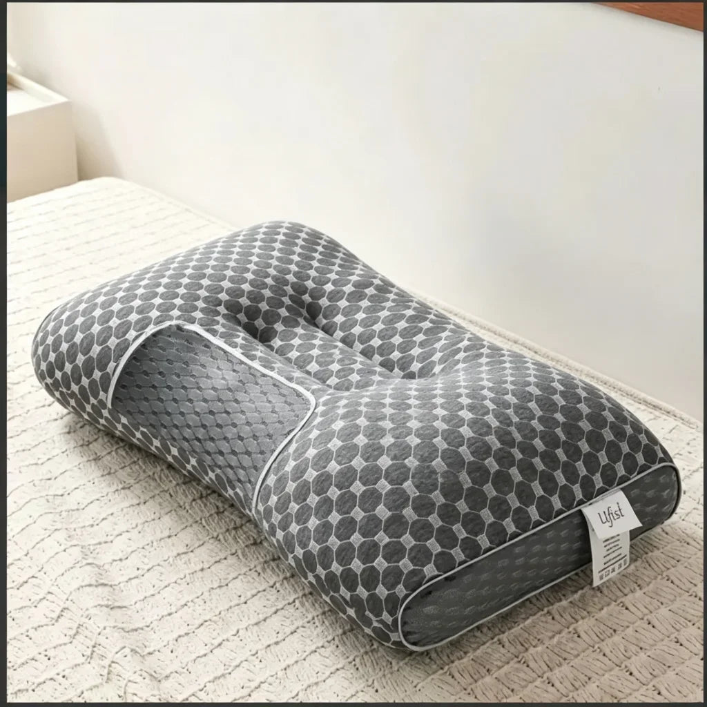 A gray ergonomic contour neck pillow with a honeycomb pattern resting on a light-colored textured surface.