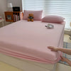 A pink fitted bed sheet cover is draped over a bed, with a small teddy bear and silver rings visible on the surface.