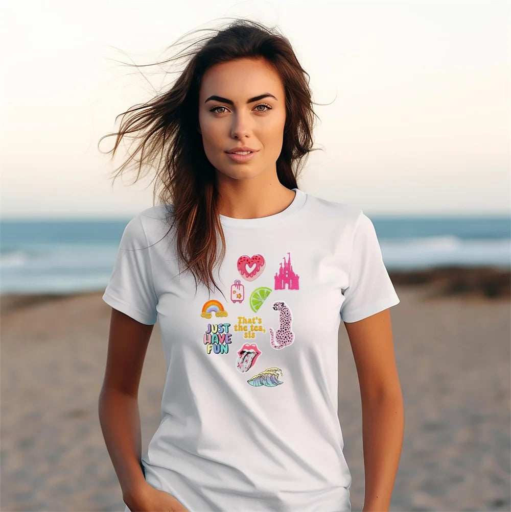 A woman models a white t-shirt featuring assorted cartoon embroidery patches on a beach at sunset.