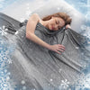A woman is lying down under a gray cooling quilted summer blanket surrounded by snowflakes.