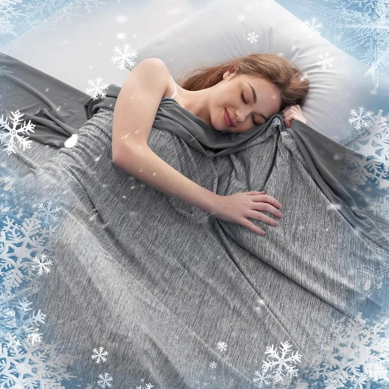 A woman is lying down under a gray cooling quilted summer blanket surrounded by snowflakes.