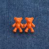 Two small orange bear button pins placed on a blue denim fabric.