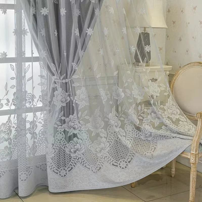 Sheer gray floral lace curtain draped over a chair in a bright room.