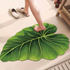 A person's foot is resting on a large green leaf-shaped quick-dry bathroom mat.