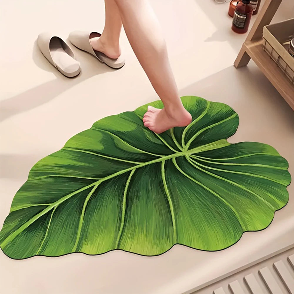 A person's foot is resting on a large green leaf-shaped quick-dry bathroom mat.