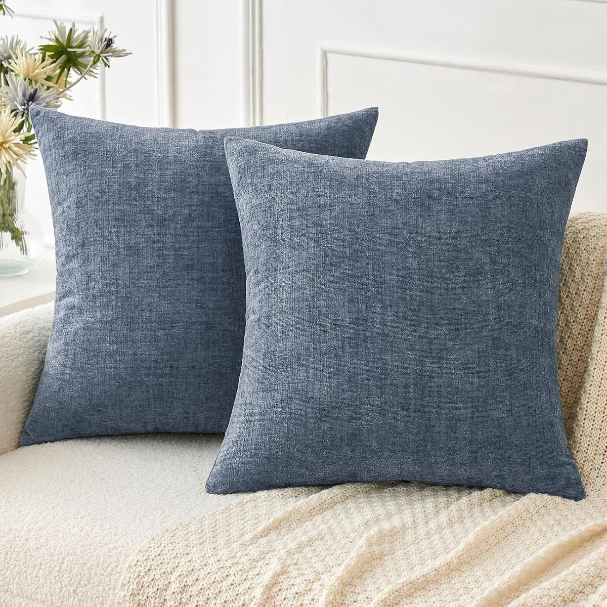 A solid blue gray chenille throw pillow cover resting on a light beige knitted blanket.